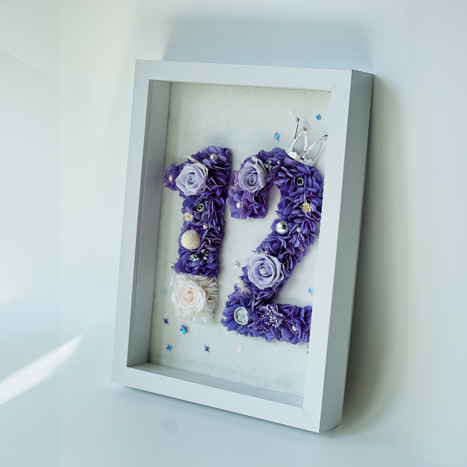 Custom number floral artwork featuring preserved roses and hydrangeas in regal purple and white, accented with sparkling embellishments and a tiara. Perfect for commemorating milestones.