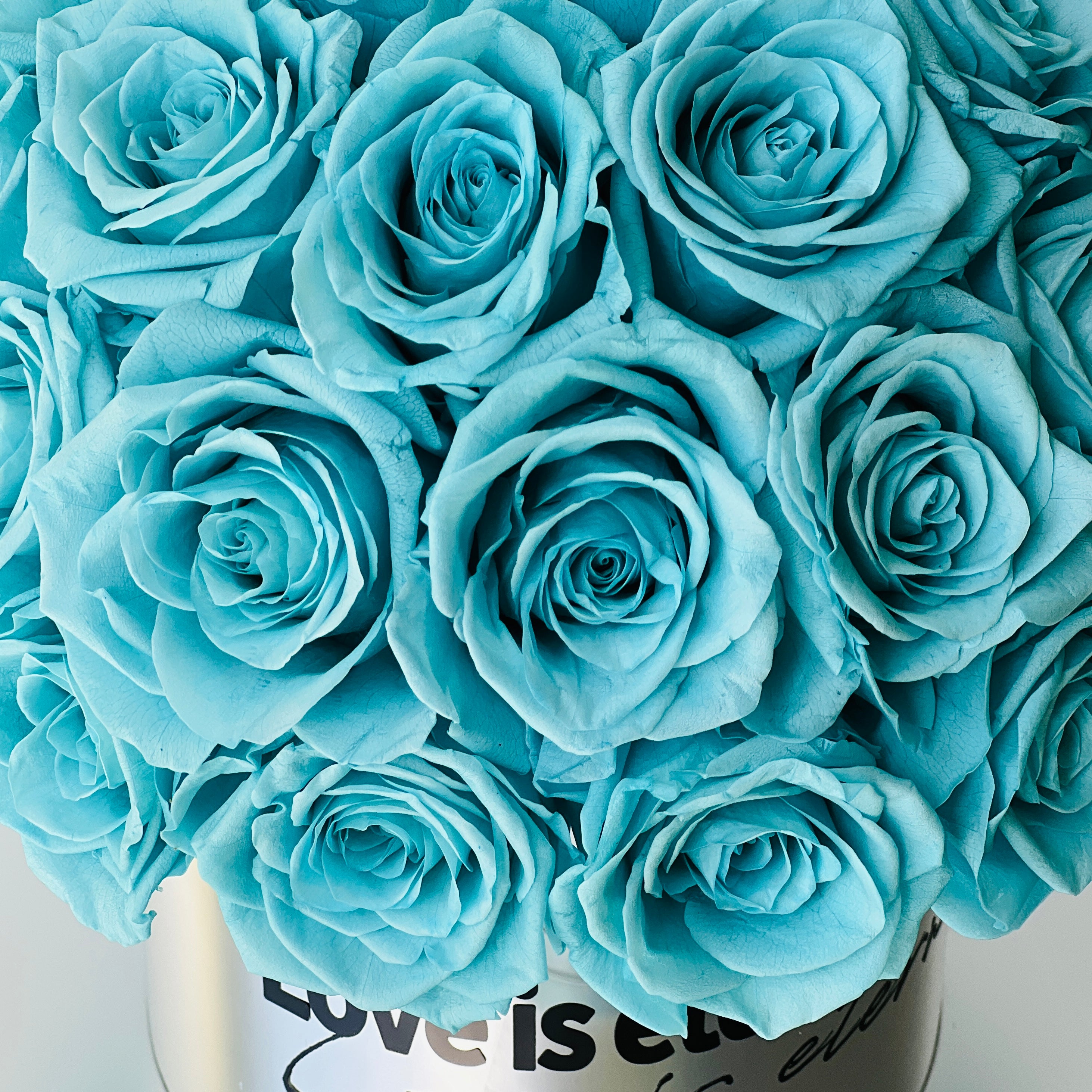 The Tiffany Blue Rose Hatbox features preserved roses on a sleek grey base inscribed with "love is eternal." This serene eternity rose arrangement offers a modern statement of enduring affection, perfect for adding tranquility to any space or as a heartfelt gift.