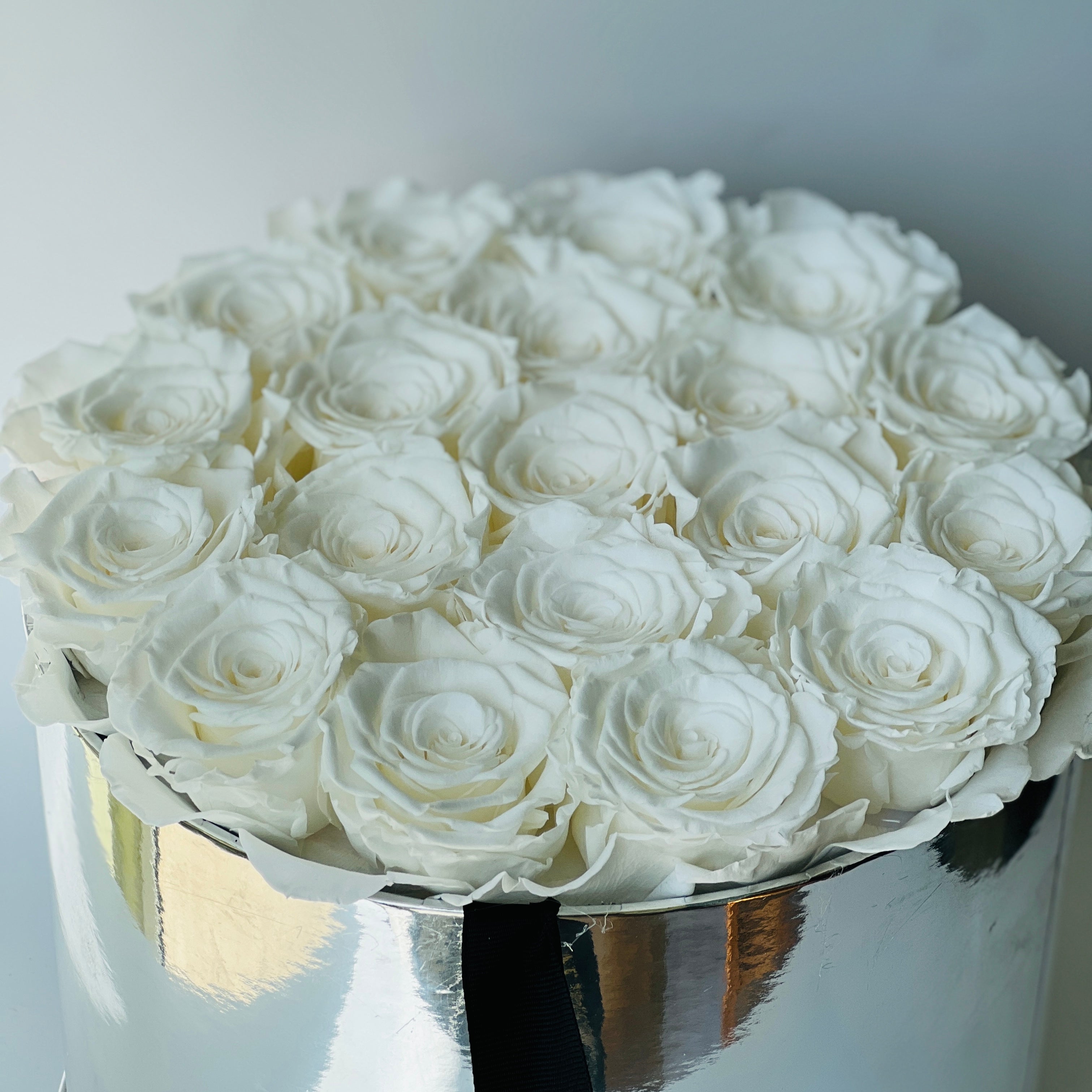 The White Rose Hatbox features preserved white roses elegantly arranged on a reflective silver base, offering a statement of purity and luxury. This timeless eternity rose gift is ideal for adding a serene and classic touch to any space, perfect for special occasions.