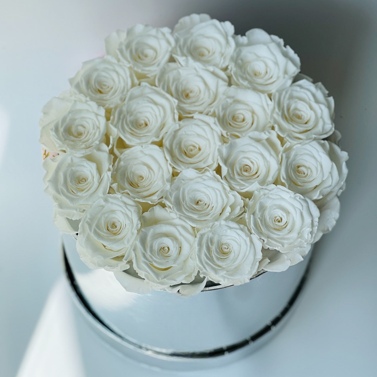 The White Rose Hatbox features preserved white roses elegantly arranged on a reflective silver base, offering a statement of purity and luxury. This timeless eternity rose gift is ideal for adding a serene and classic touch to any space, perfect for special occasions.