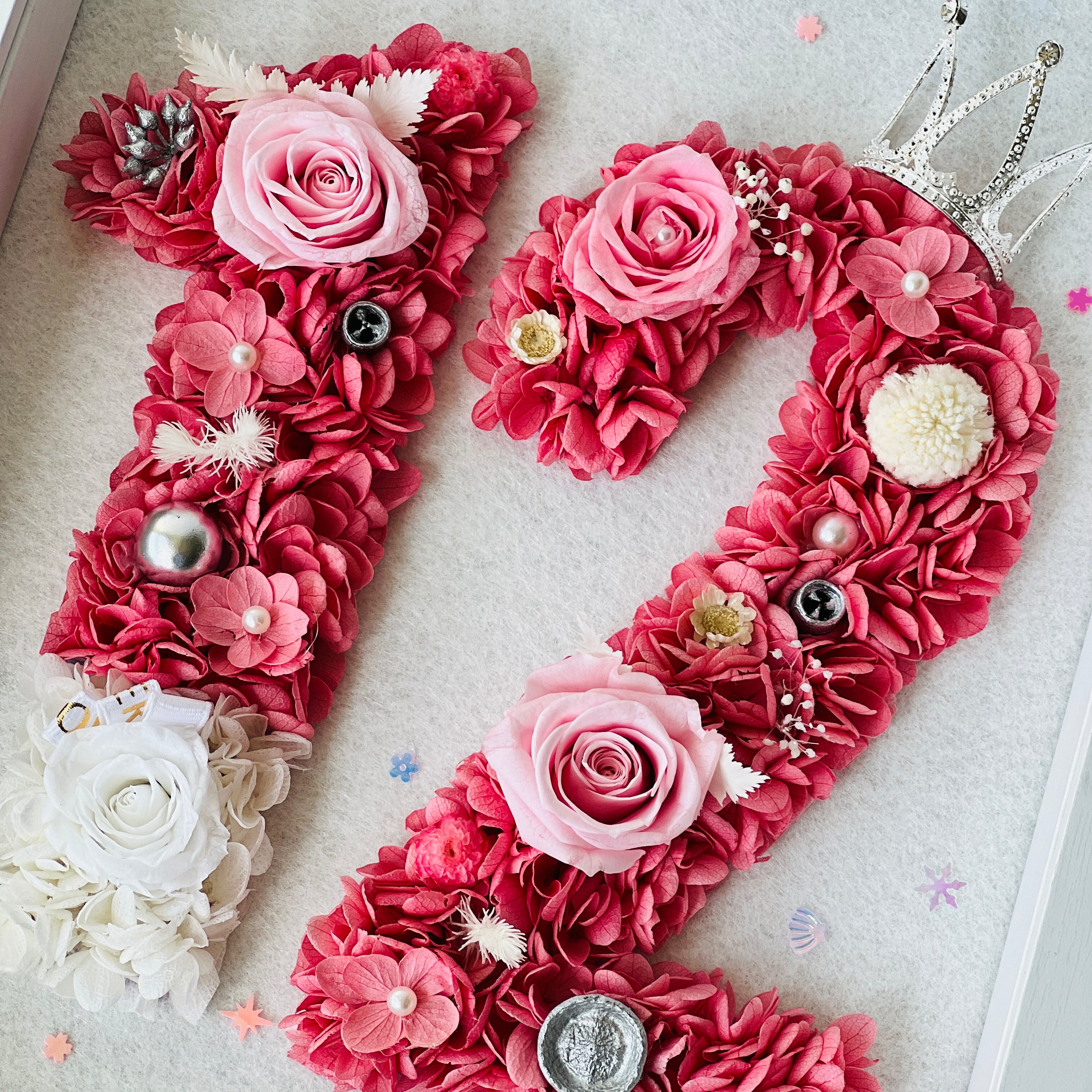 Custom number floral artwork featuring preserved roses and hydrangeas in pink hues, accented with sparkling embellishments and a tiara. Ideal for gifting or decor.