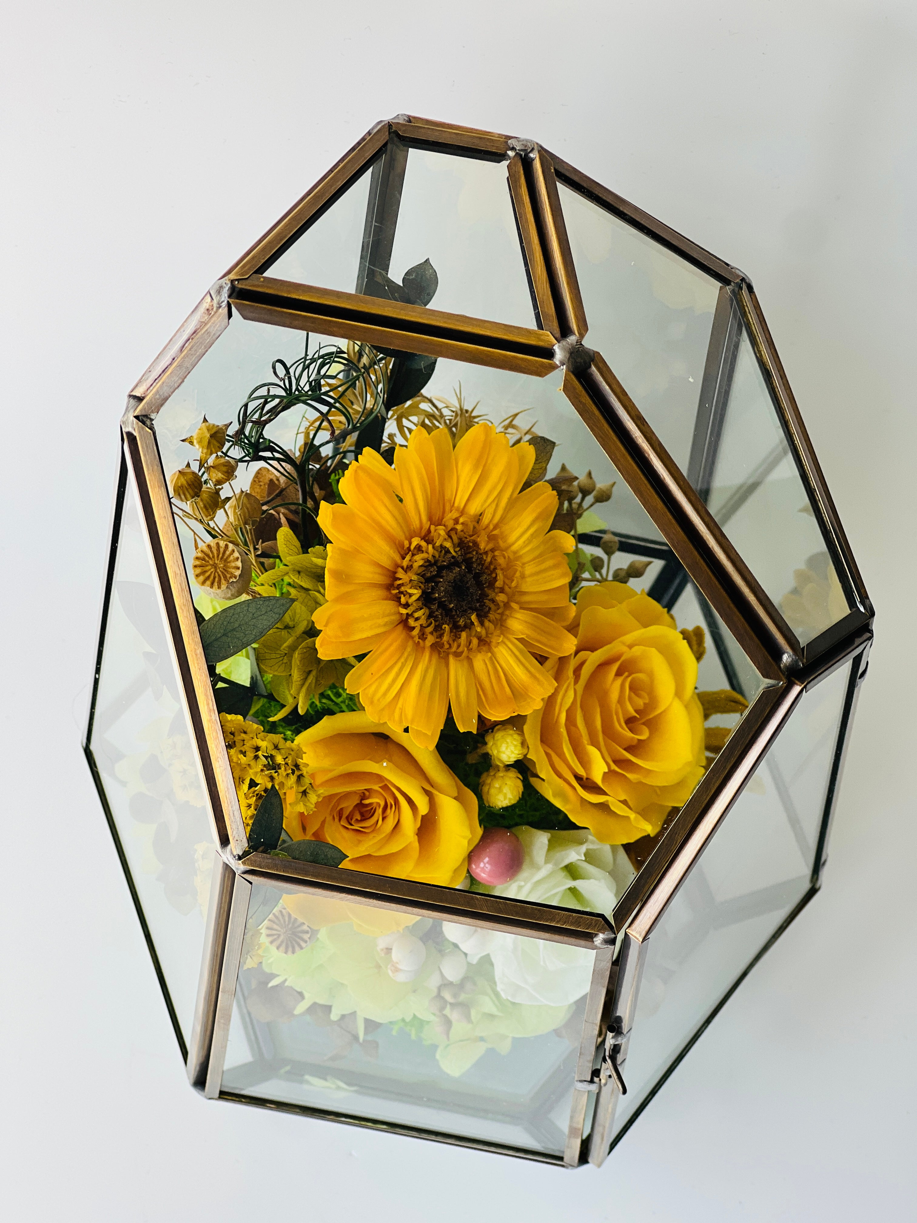 Sunshine and Serenity preserved floral arrangement featuring sunny yellow roses, a cheerful sunflower, and delicate white roses in a geometric acrylic terrarium. A perfect eternity rose gift to brighten any space.