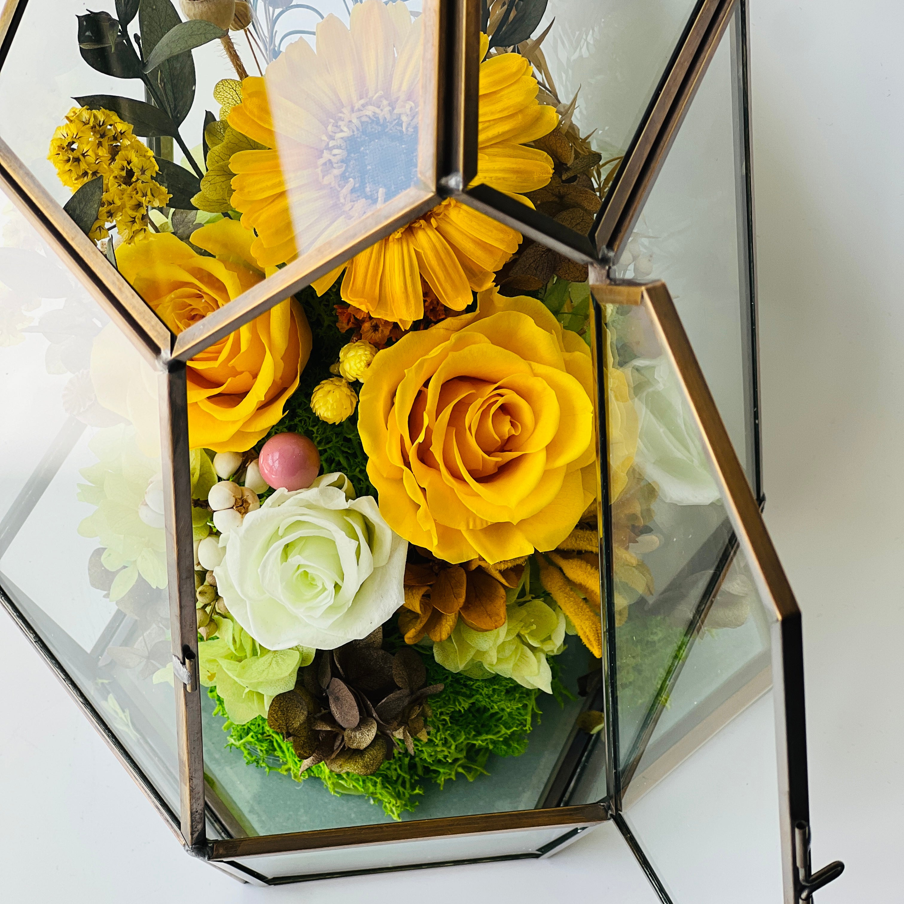 Sunshine and Serenity preserved floral arrangement featuring sunny yellow roses, a cheerful sunflower, and delicate white roses in a geometric acrylic terrarium. A perfect eternity rose gift to brighten any space.