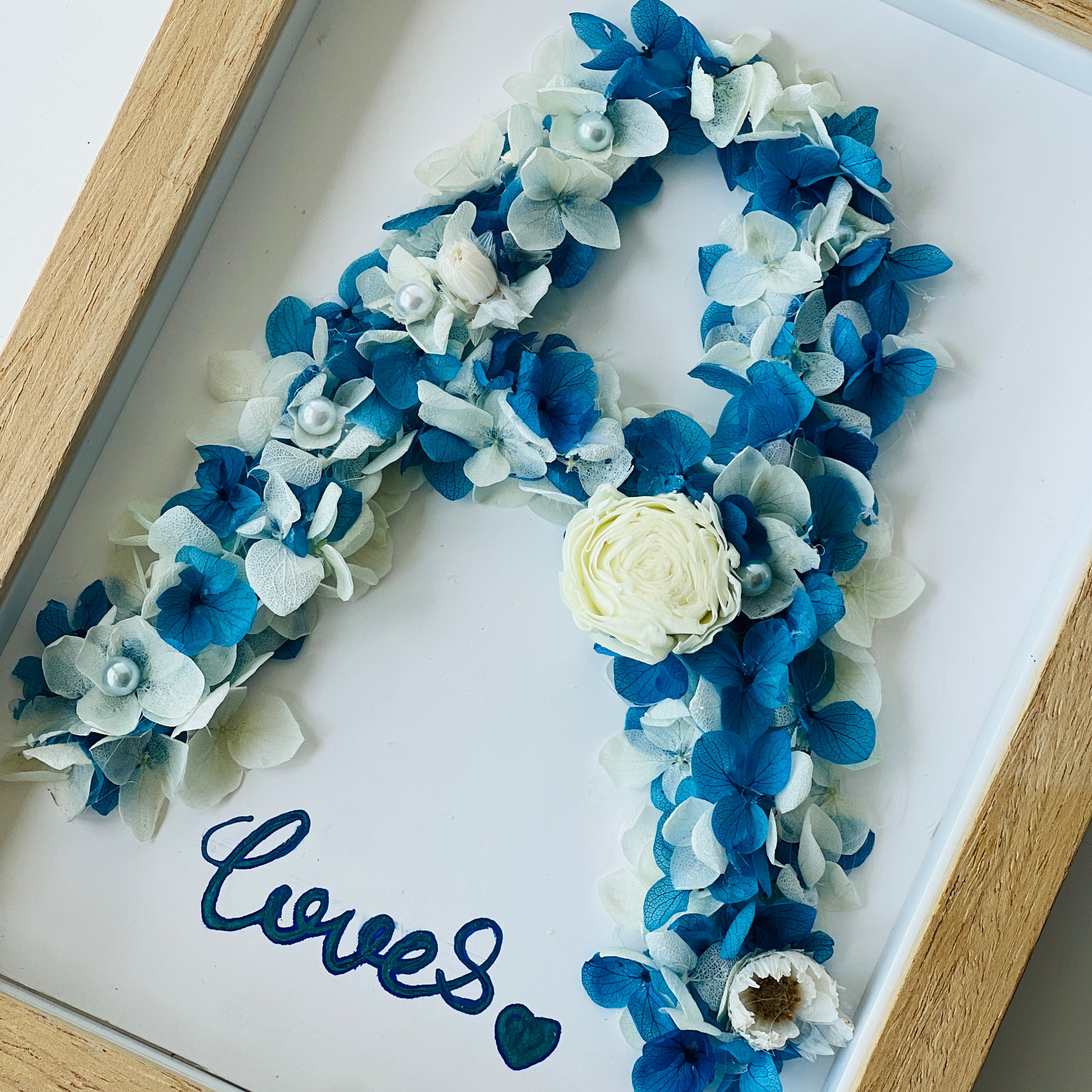 Preserved floral letter display featuring blue and white hydrangeas, accented with pearls and a white rose. Perfect for personalized gifting or home decor.