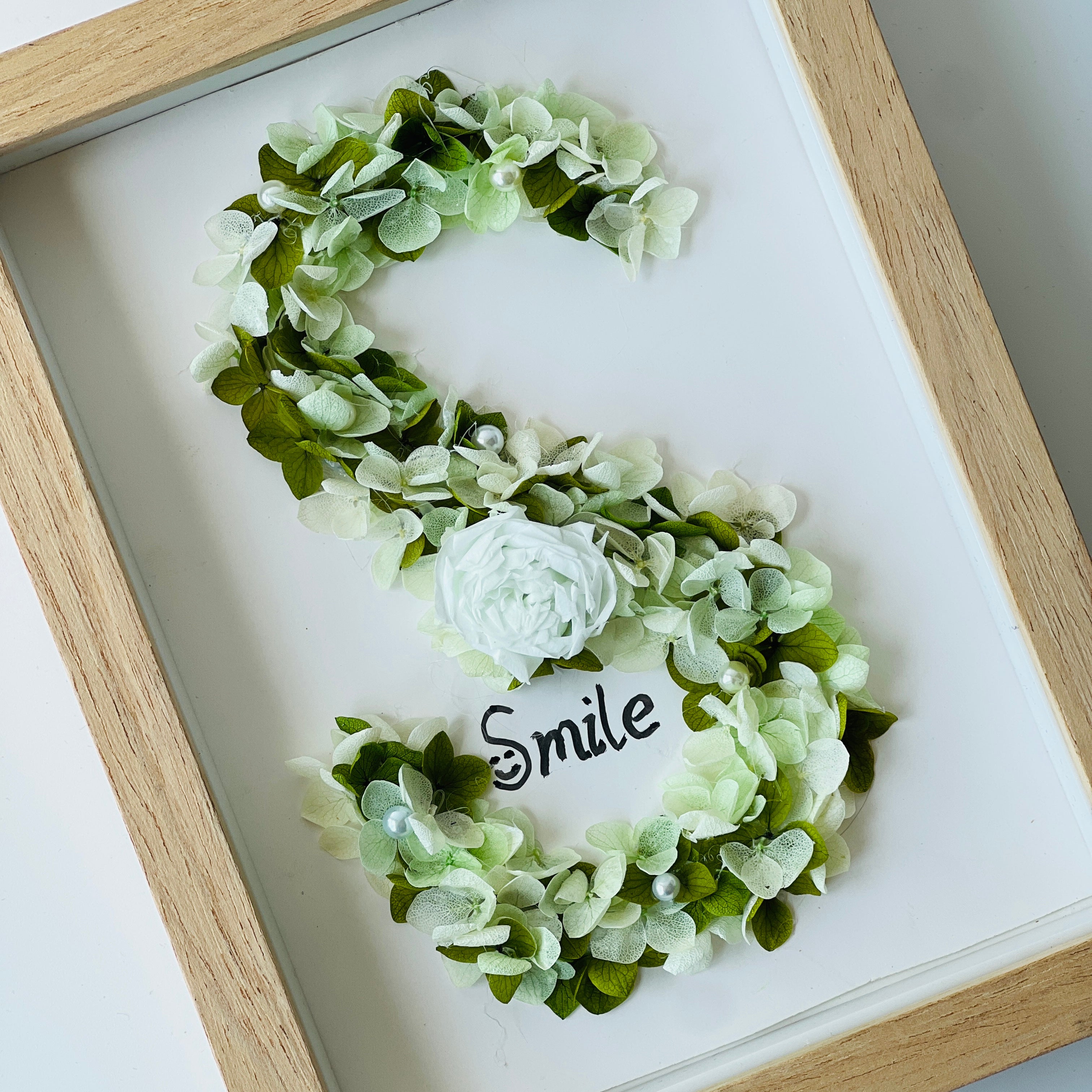 Serene preserved floral letter art featuring a white rose with soft green hydrangeas and pearl accents, framed in natural wood—a perfect calming gift.