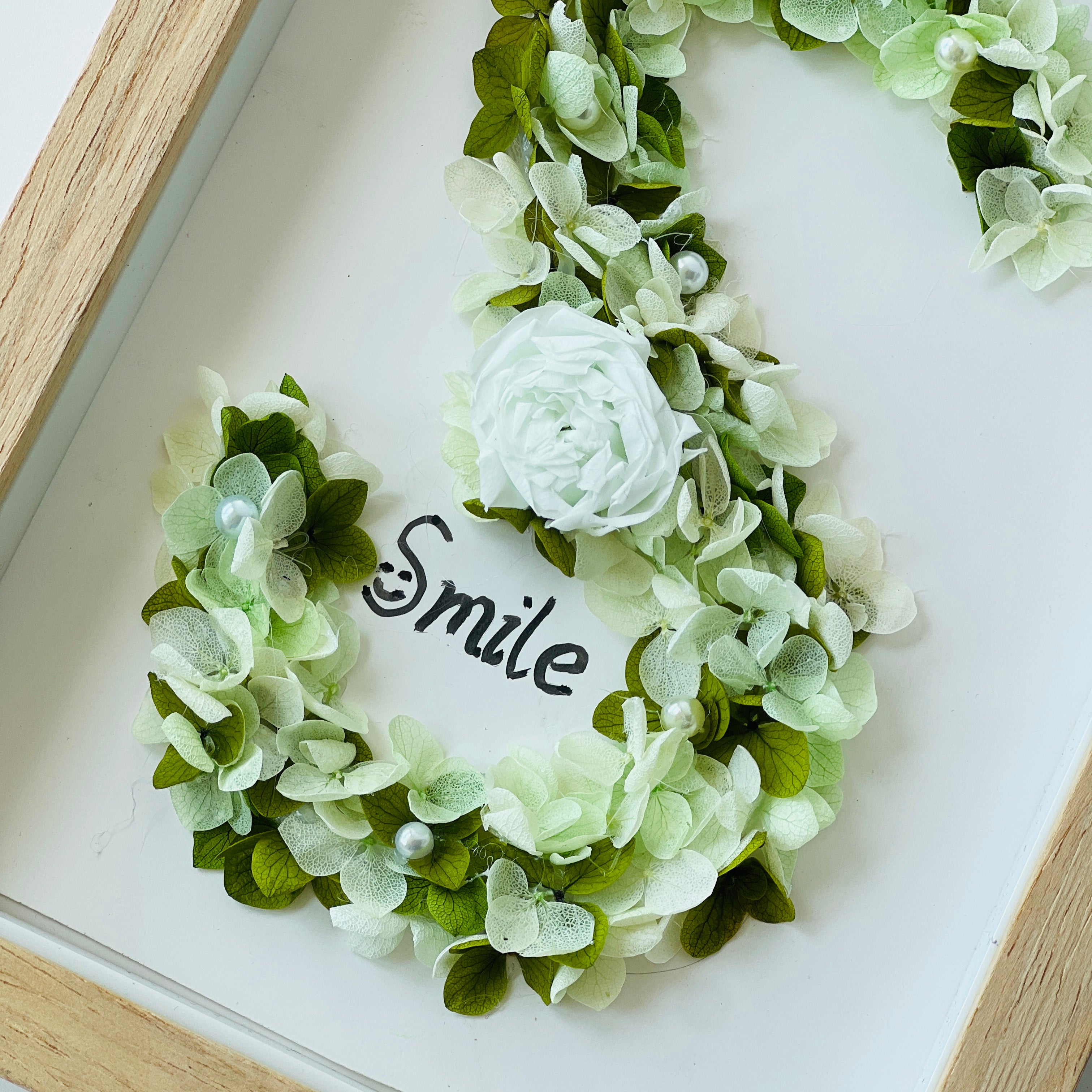 Serene preserved floral letter art featuring a white rose with soft green hydrangeas and pearl accents, framed in natural wood—a perfect calming gift.