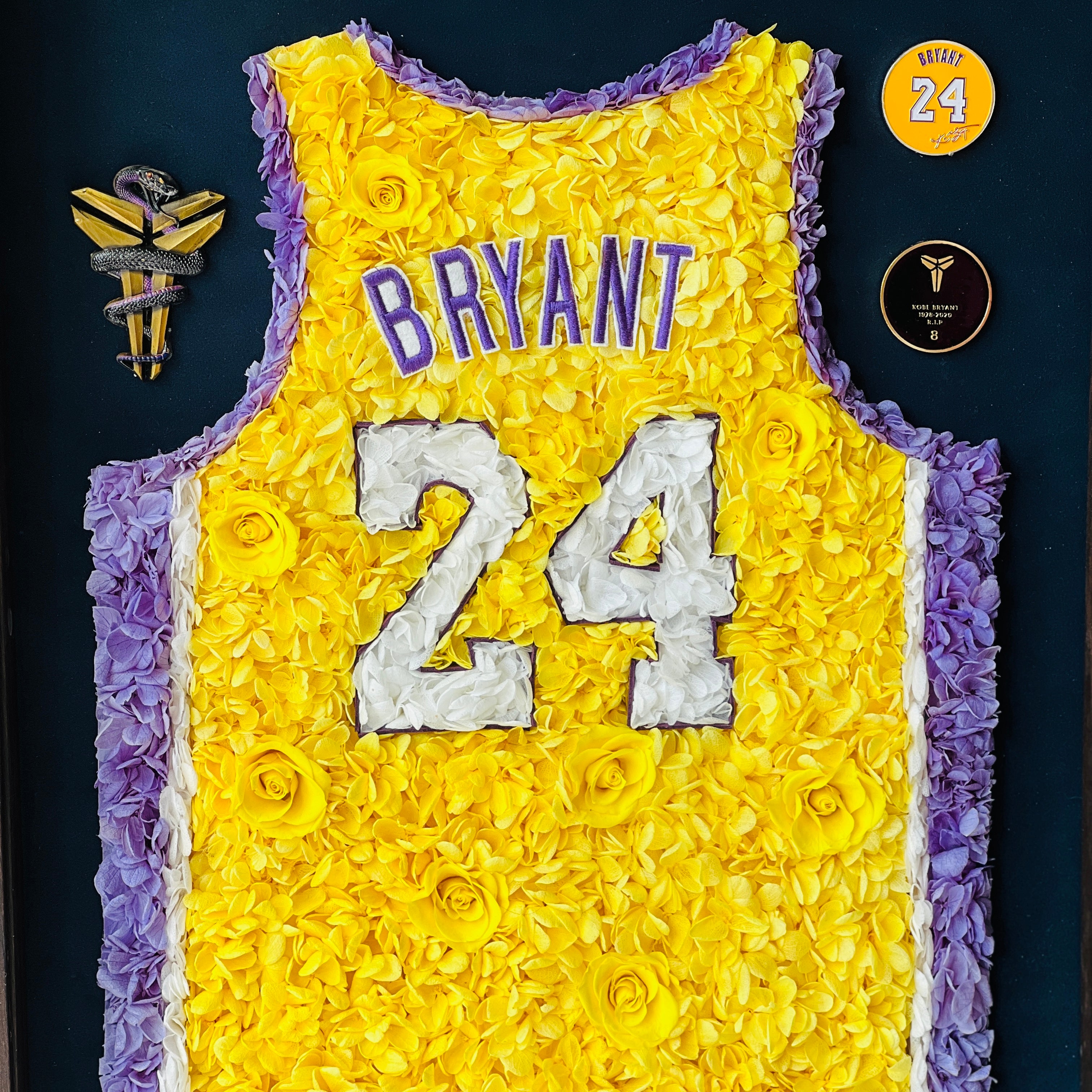 Preserved floral tribute to Kobe Bryant's iconic number 24 jersey, featuring roses and hydrangeas in yellow and purple, framed in dark wood. A perfect piece for collectors and enthusiasts.