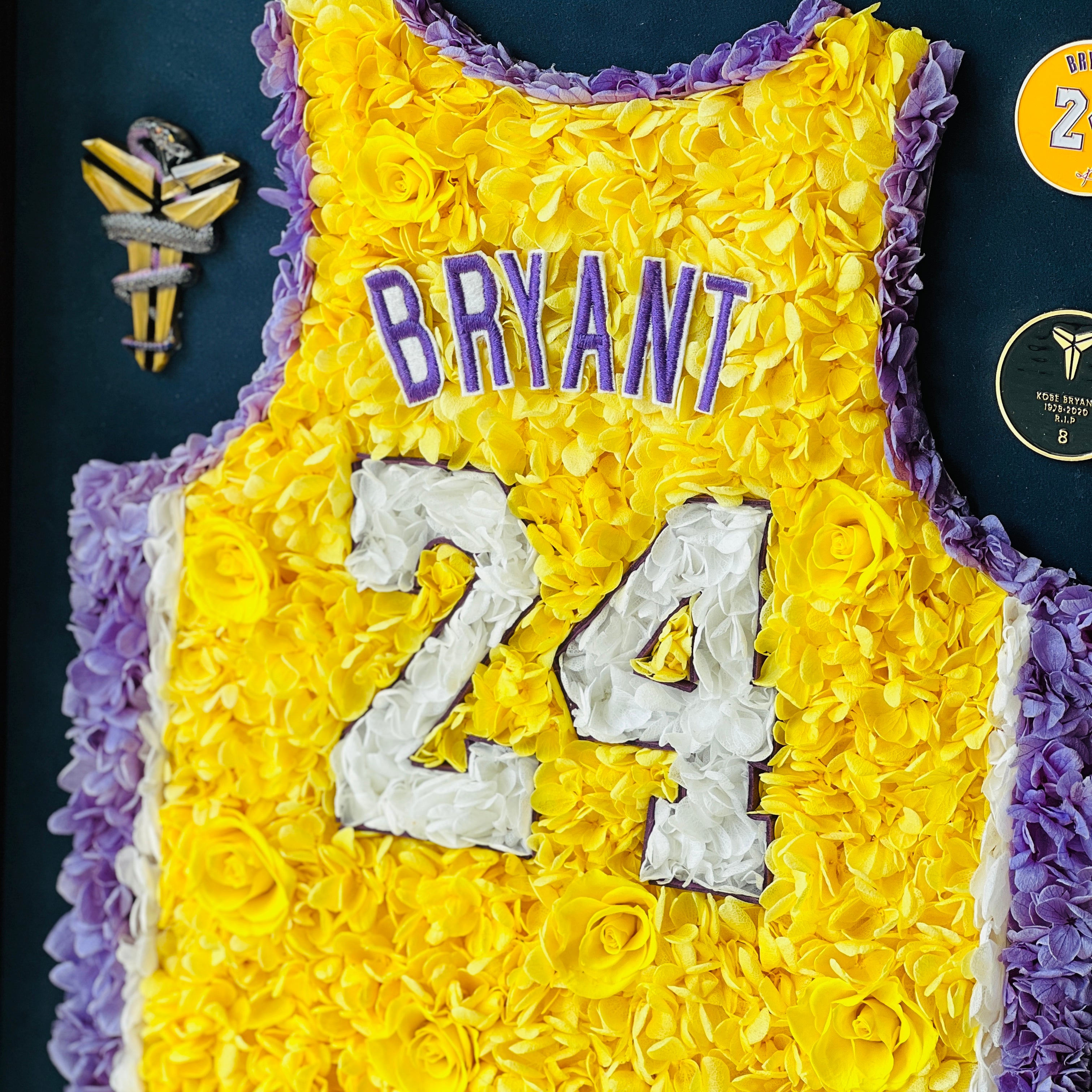 Preserved floral tribute to Kobe Bryant's iconic number 24 jersey, featuring roses and hydrangeas in yellow and purple, framed in dark wood. A perfect piece for collectors and enthusiasts.