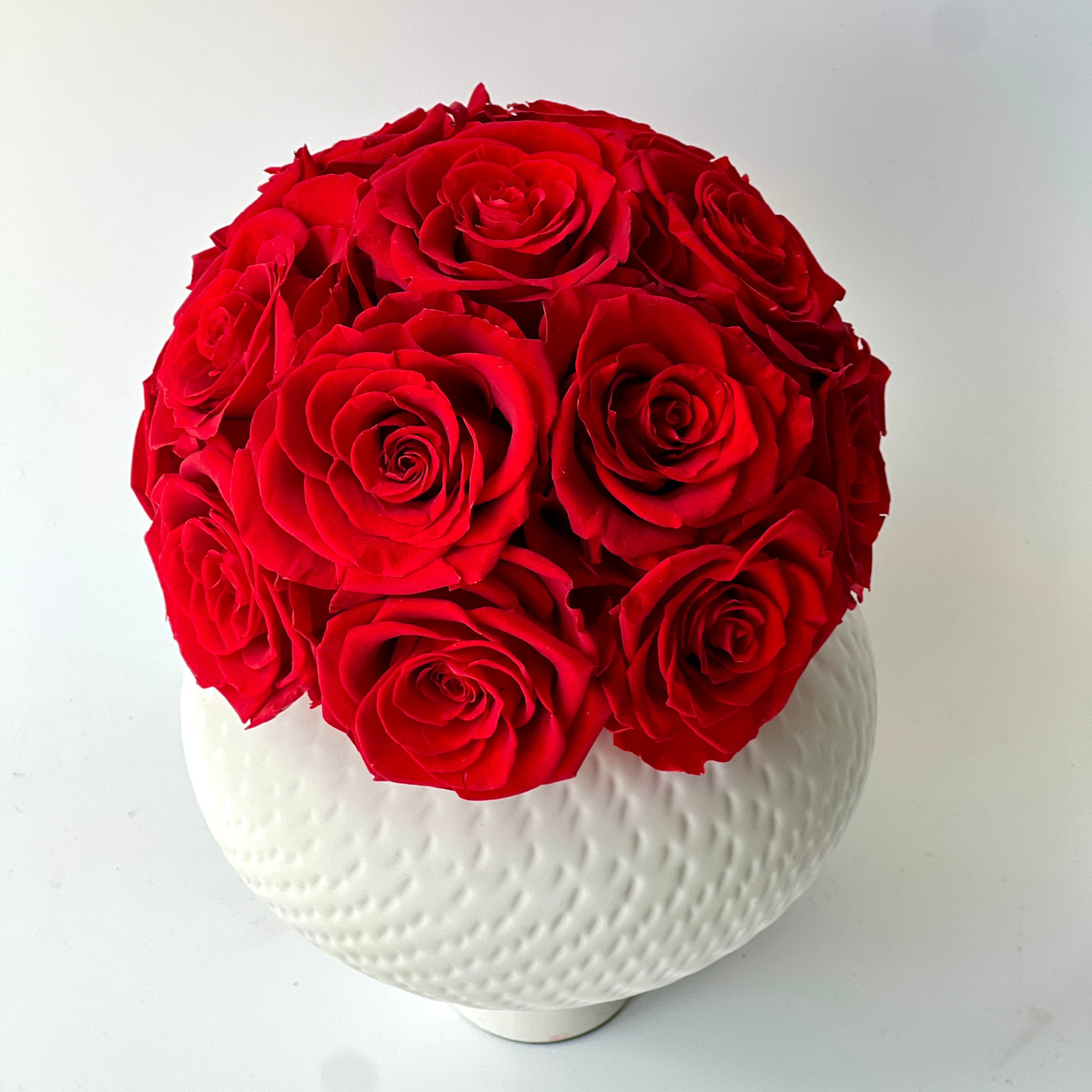 Deep red preserved roses in a textured white vase create a striking, elegant centerpiece. Maintenance-free and perfect for adding lasting beauty to any space.