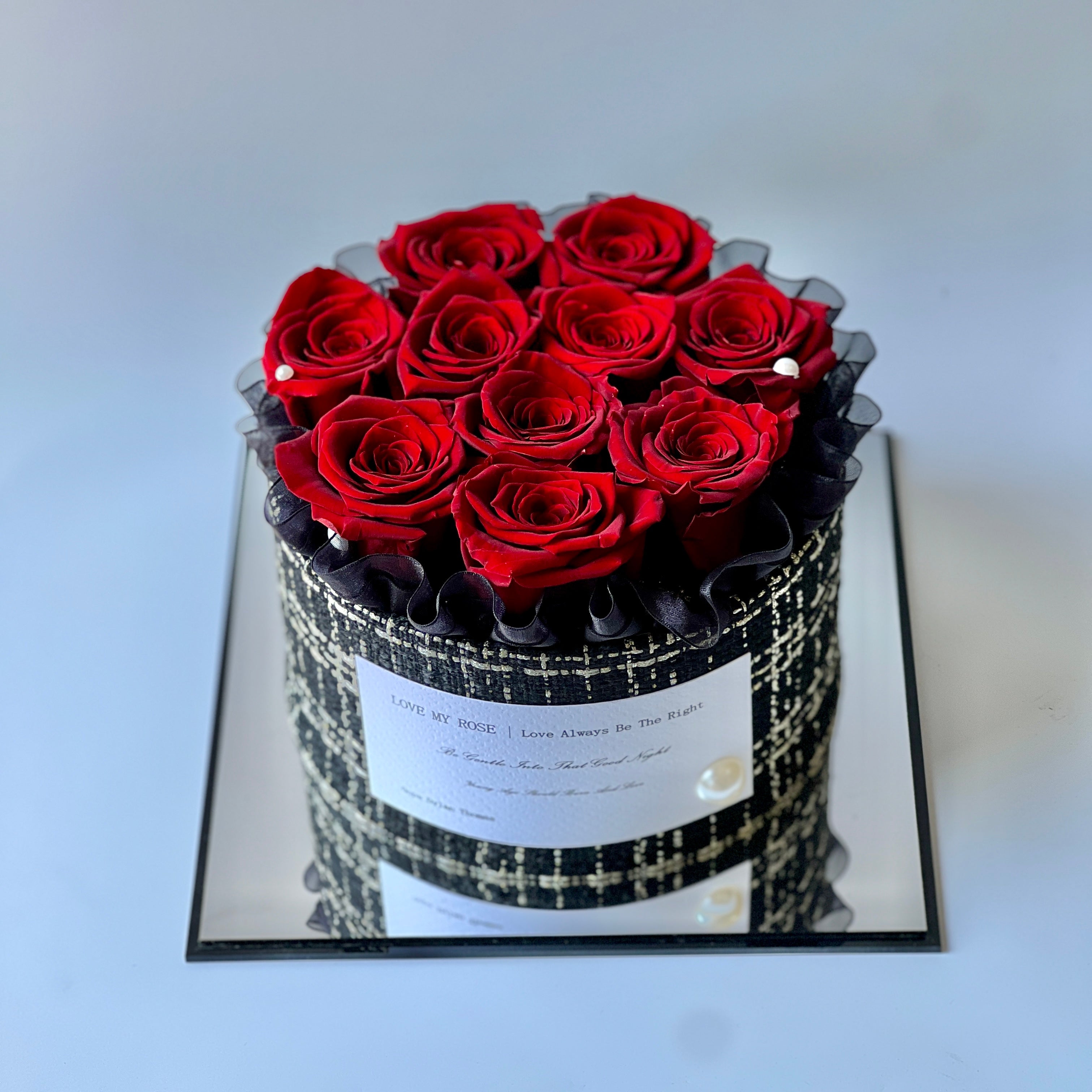 The Crimson Elegance preserved flower arrangement features deep red roses encased in a luxurious black and white patterned box, adorned with pearl accents. A timeless eternity rose gift, perfect for adding romance and sophistication to any space.