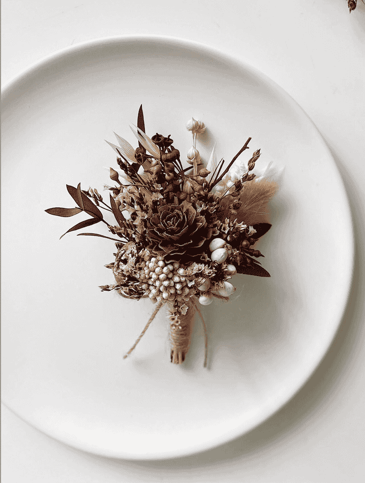 Pinecone boutonniere with dried florals on a white plate.
