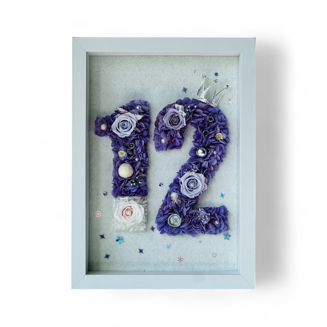 Custom number floral artwork featuring preserved roses and hydrangeas in regal purple and white, accented with sparkling embellishments and a tiara. Perfect for commemorating milestones.