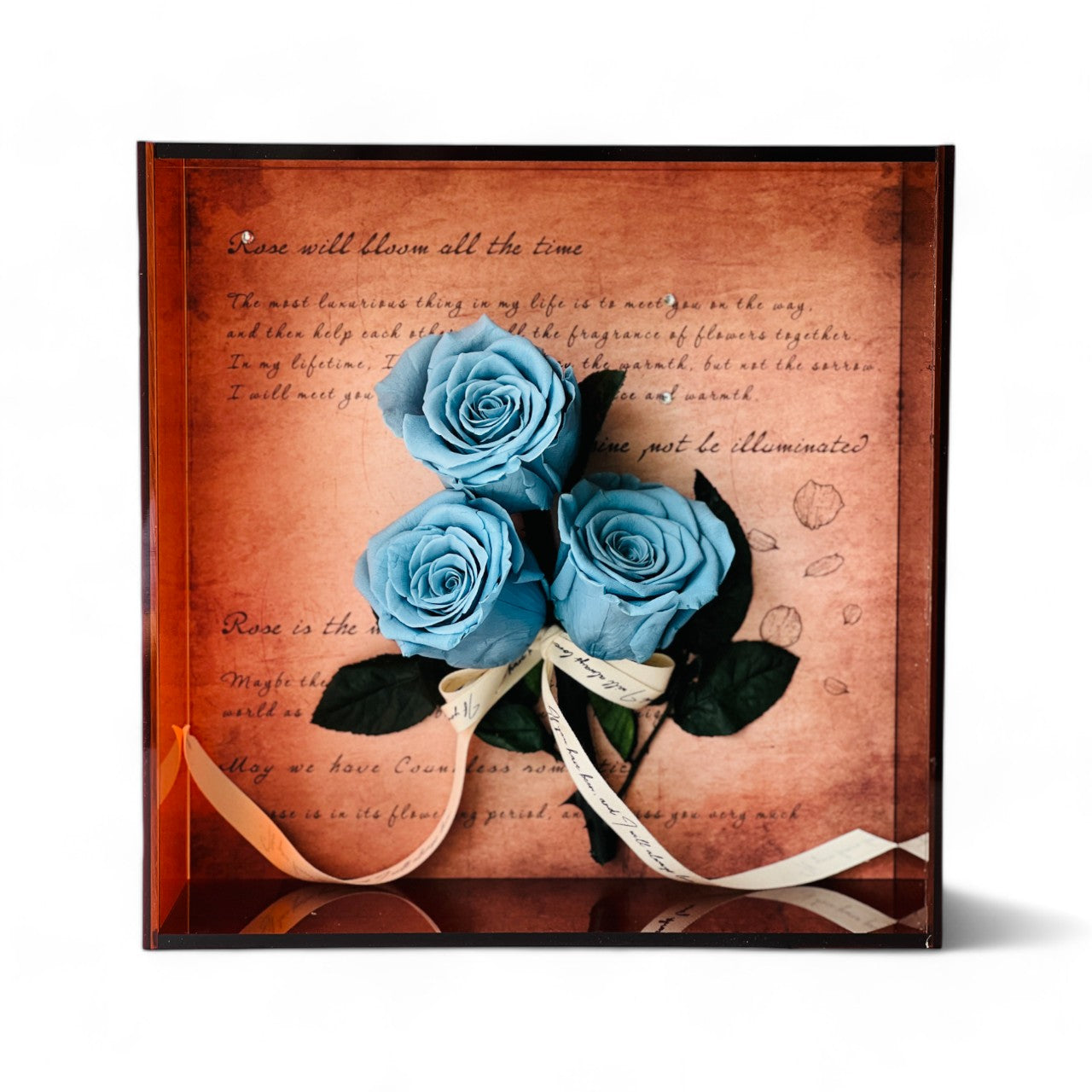 Artful display of preserved ocean blue roses set against handwritten script, wrapped in vintage ribbon within a deep copper frame. Perfect as an elegant eternity rose gift.