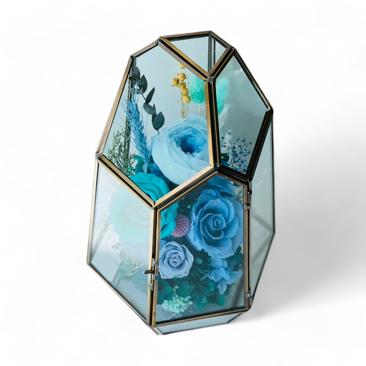 Exquisite Ocean Breeze preserved floral terrarium featuring deep ocean blue roses and hydrangeas, accented with greenery and pink florals in a modern geometric vessel. Perfect as a timeless eternity rose gift.