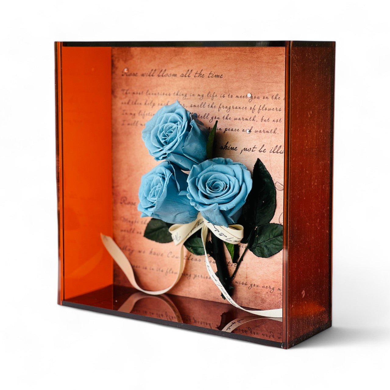 Artful display of preserved ocean blue roses set against handwritten script, wrapped in vintage ribbon within a deep copper frame. Perfect as an elegant eternity rose gift.