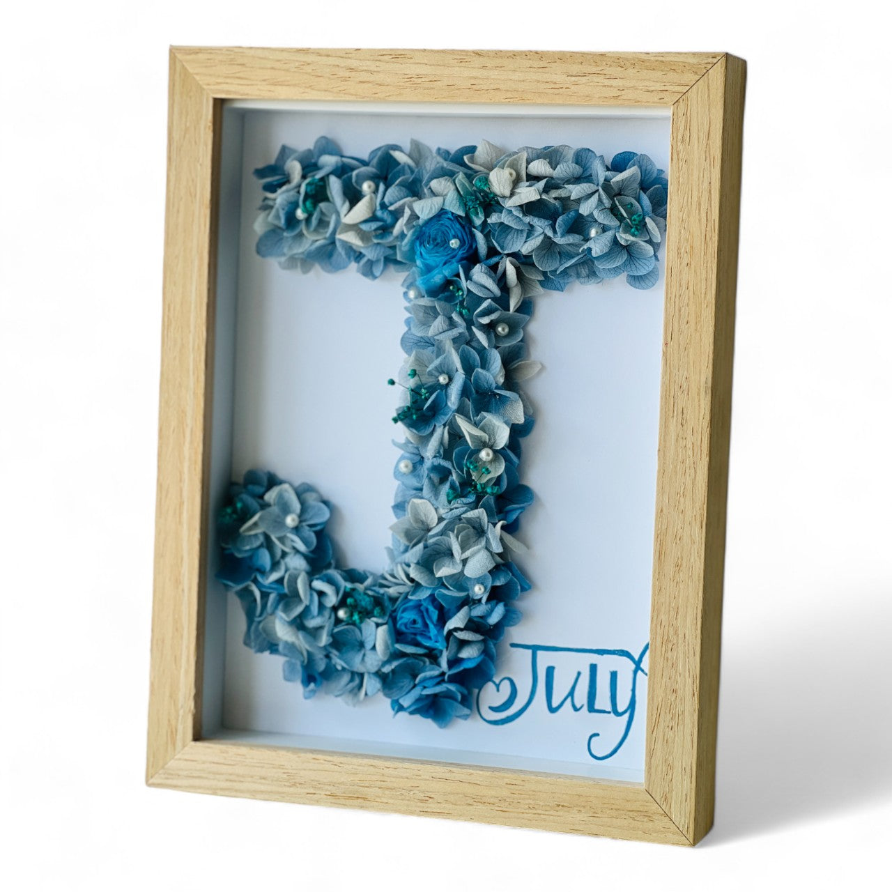 Crafted initial-shaped preserved floral letter art featuring blue and white hydrangeas, with a white rose and pearl accents, framed in natural wood—a personalized gift.