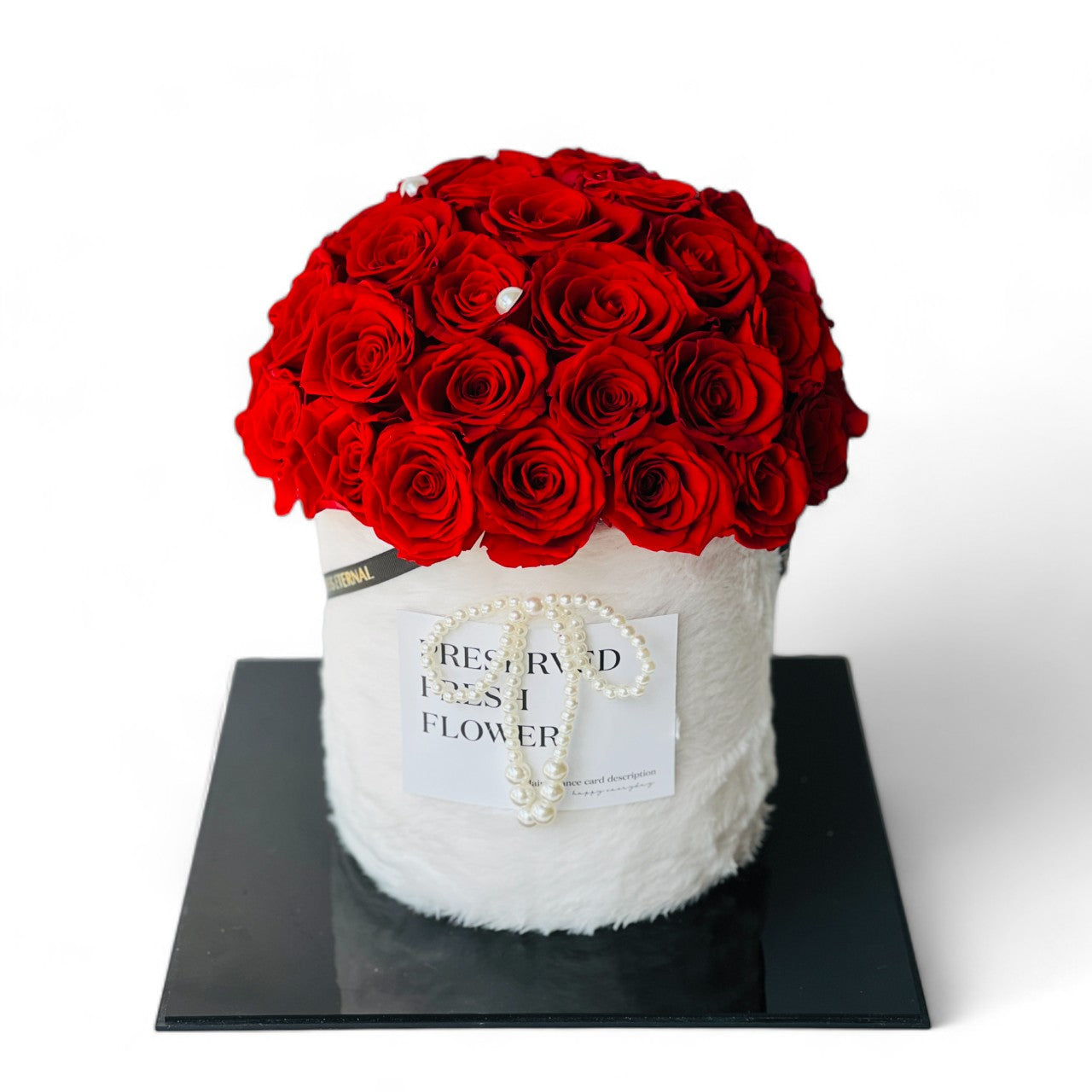 The Red Rose Dome features preserved red roses elegantly arranged atop a chic white hatbox, adorned with a pearl accent. This timeless eternity rose gift is perfect for expressing lasting love and adding a touch of class to any decor.