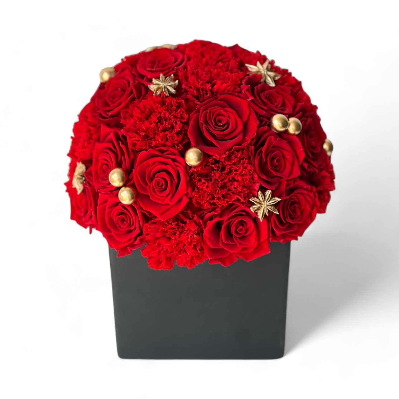 The Regal Red preserved flower arrangement features deep red roses and vibrant carnations, adorned with golden pearls and star-shaped embellishments. Encased in a sleek black box, this luxurious eternity rose gift is perfect for special occasions or as a dramatic centerpiece, celebrating timeless beauty and sophistication year-round.