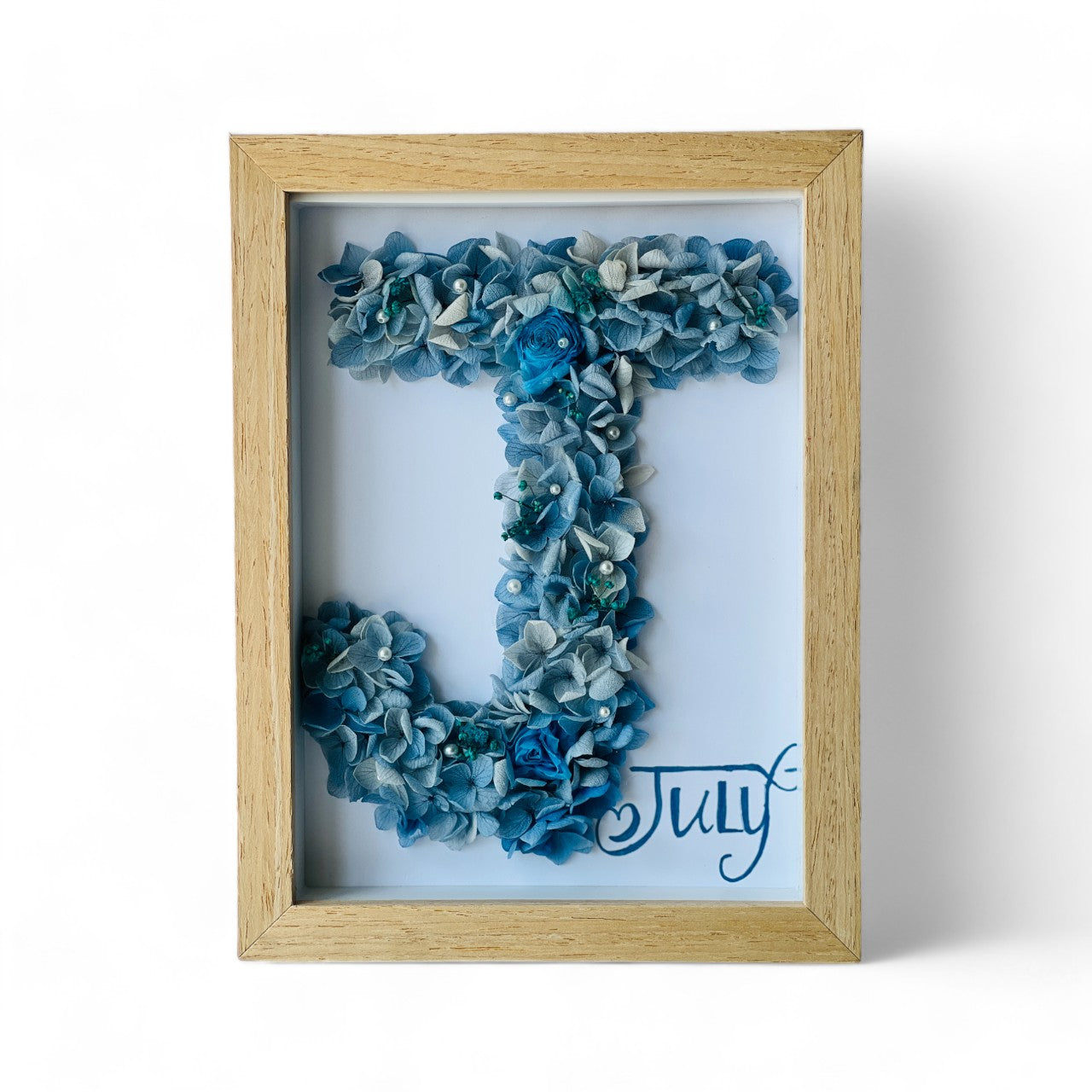 Crafted initial-shaped preserved floral letter art featuring blue and white hydrangeas, with a white rose and pearl accents, framed in natural wood—a personalized gift.