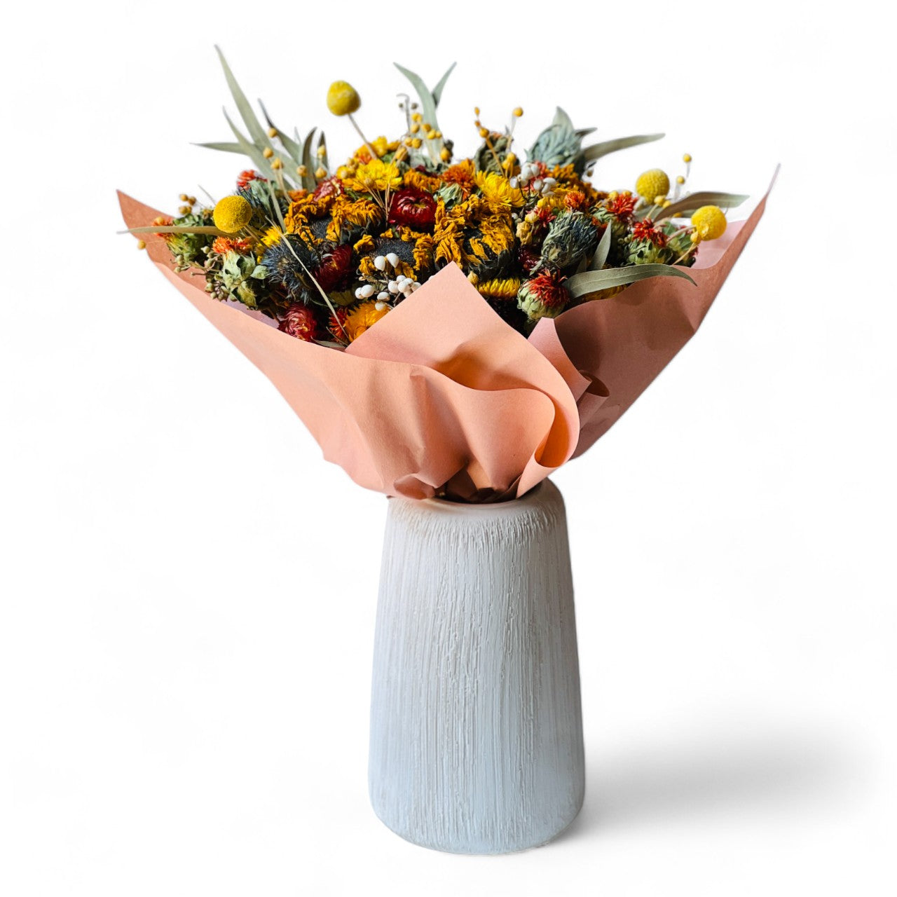 Autumn Harvest Bouquet with sunflowers, craspedia, and strawflowers in warm autumn colors. Accented by soft greenery and wrapped in peach paper, this bouquet adds rustic charm to any space, maintenance-free.