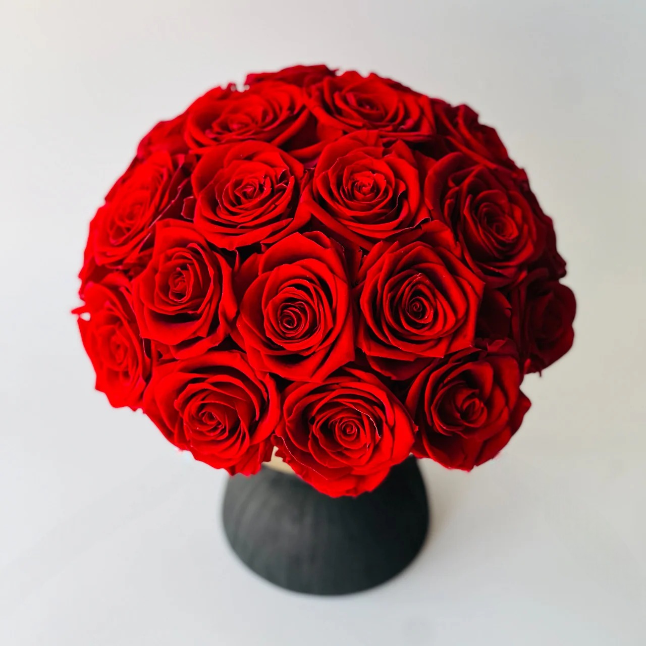 Elegant preserved red roses arranged on a two-tone pedestal vase. Maintenance-free and perfect as a dramatic centerpiece or memorable gift.