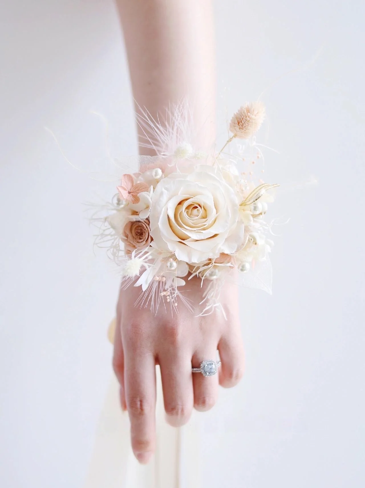 Elegant wrist corsage featuring wedding flowers with a delicate rose centerpiece, accented by dusty blue tones and French lavender. Perfect for bridesmaids, this corsage includes ranunculus flowers and adds a sophisticated touch to any wedding attire.