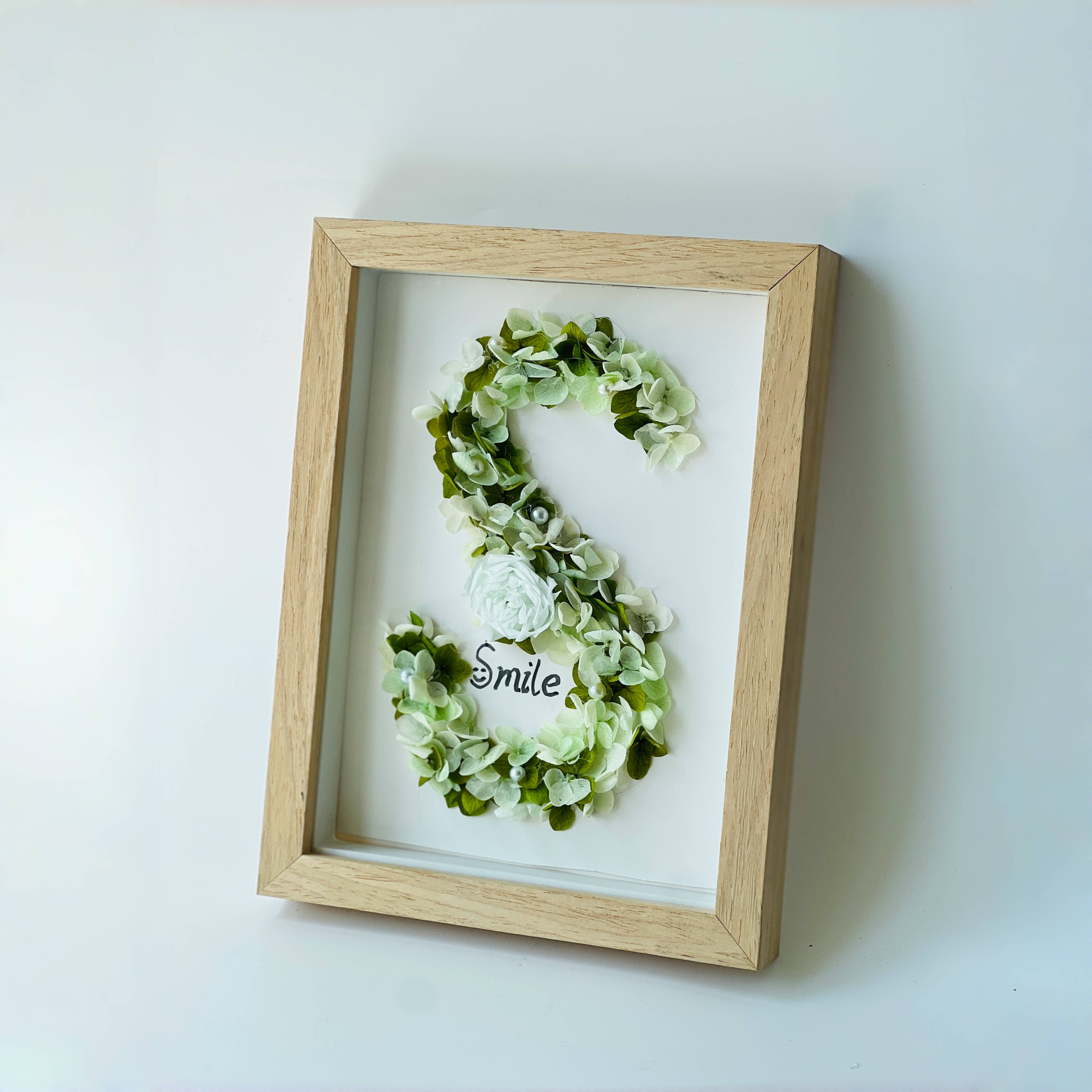 Serene preserved floral letter art featuring a white rose with soft green hydrangeas and pearl accents, framed in natural wood—a perfect calming gift.