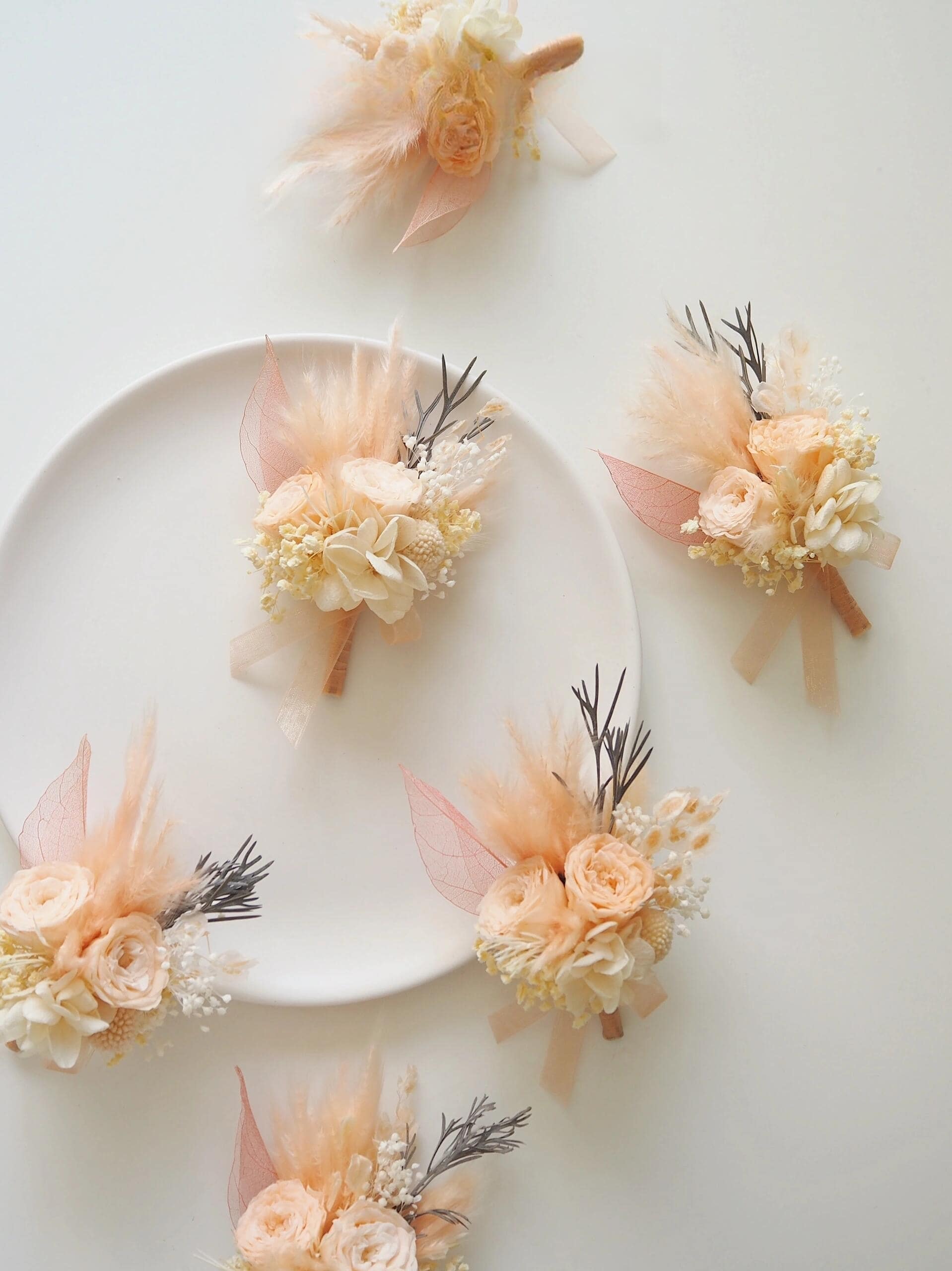 Wedding boutonniere with preserved peach ranunculus and greenery
