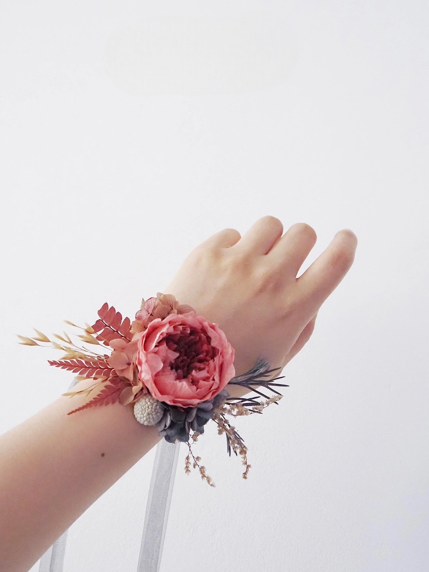 Elegant floral corsage featuring a pink peony and gray leaves.
