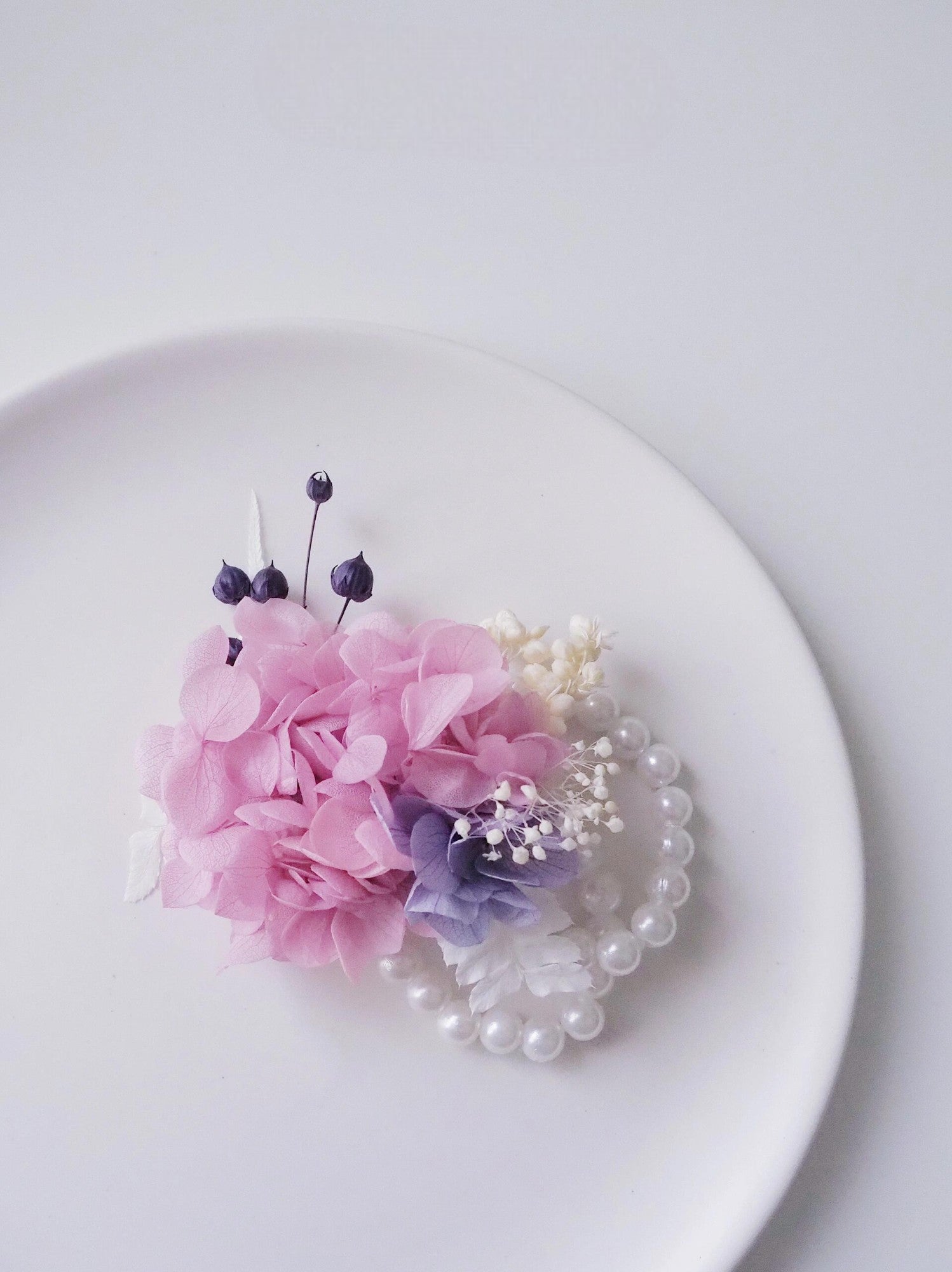 Pink hydrangea corsage with lavender accents and pearl bracelet.