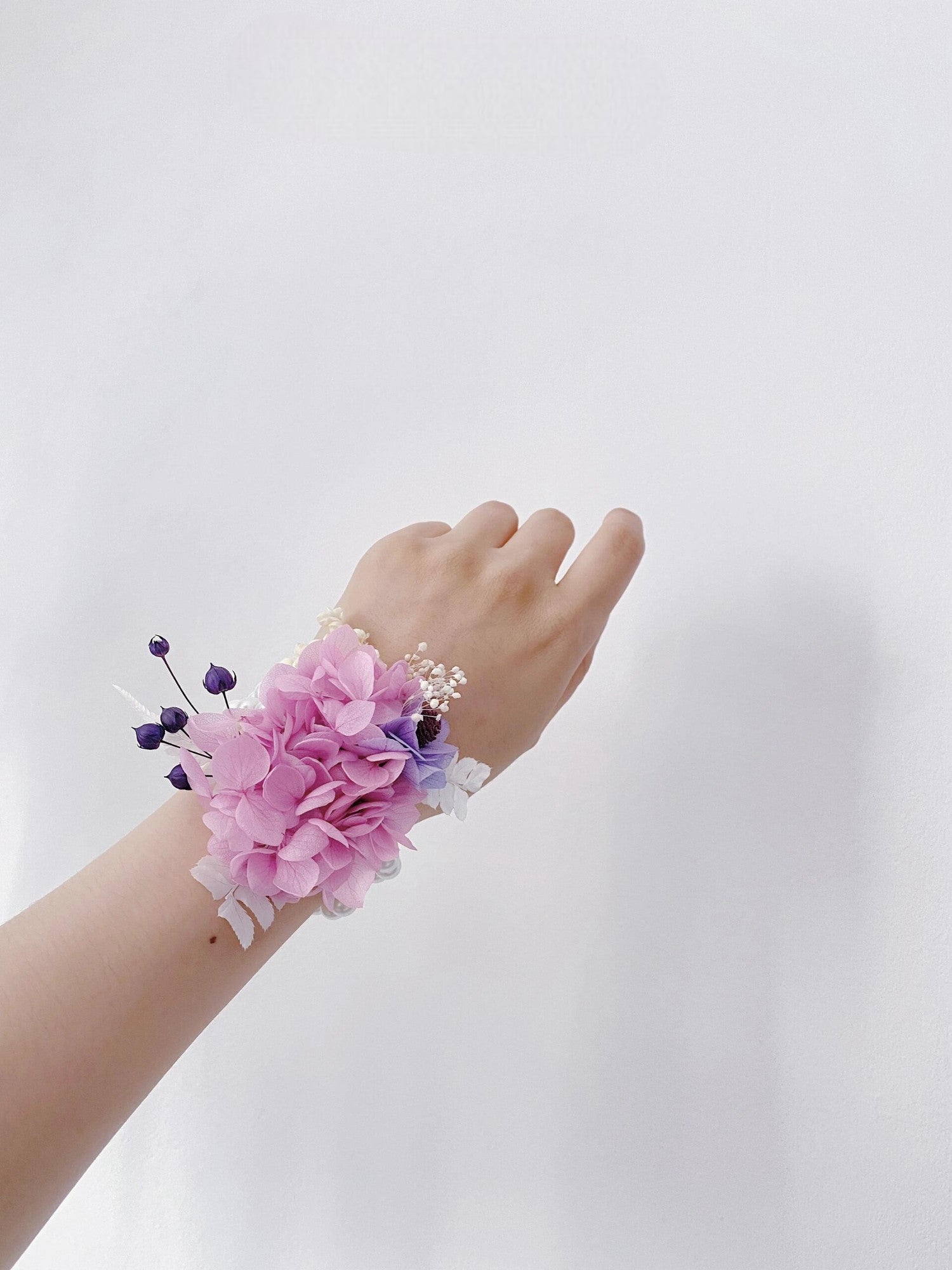 Pink hydrangea corsage with lavender accents and pearl bracelet.