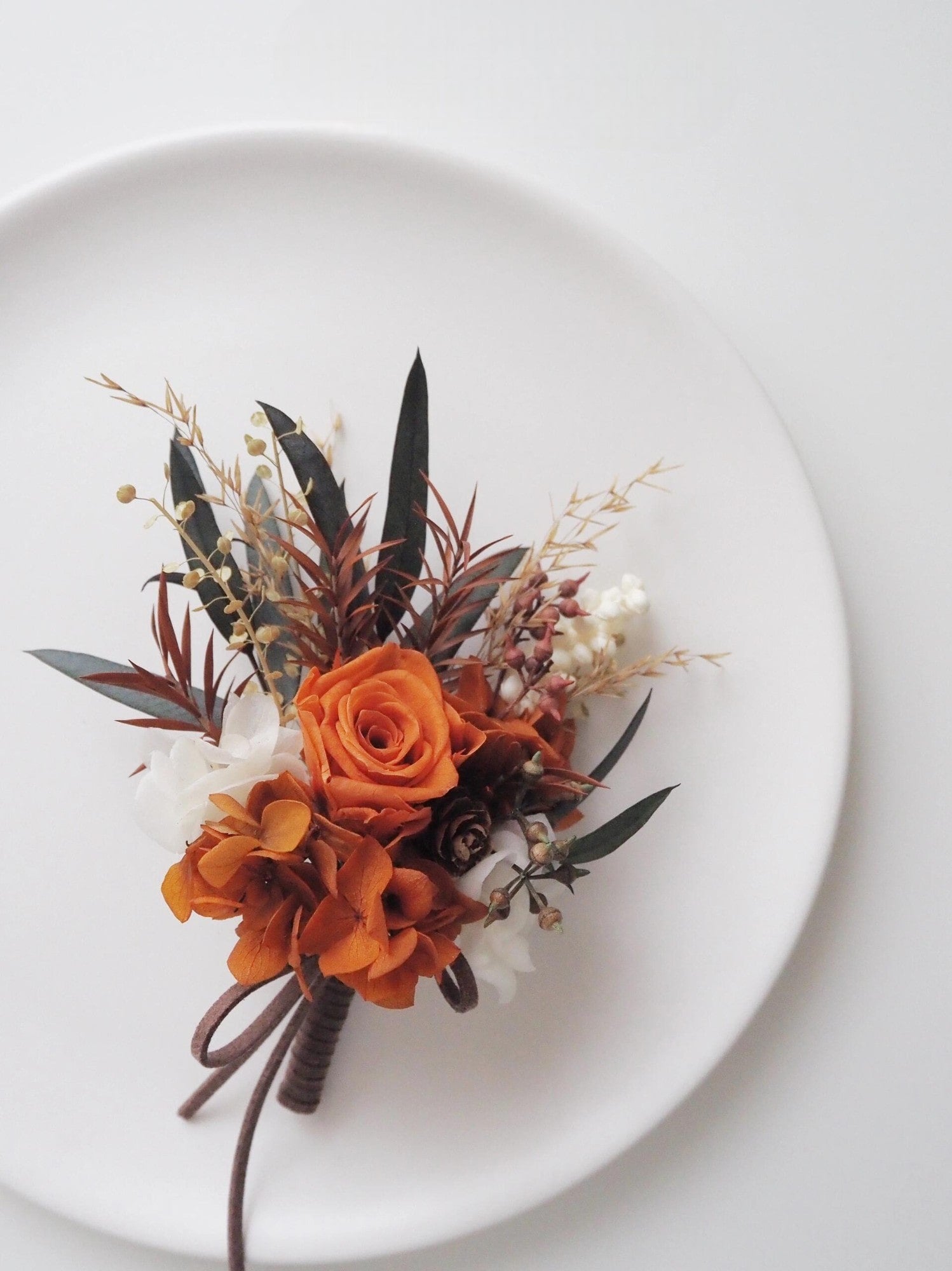 Sunset terracotta boutonniere with terracotta rose and greenery on a white plate