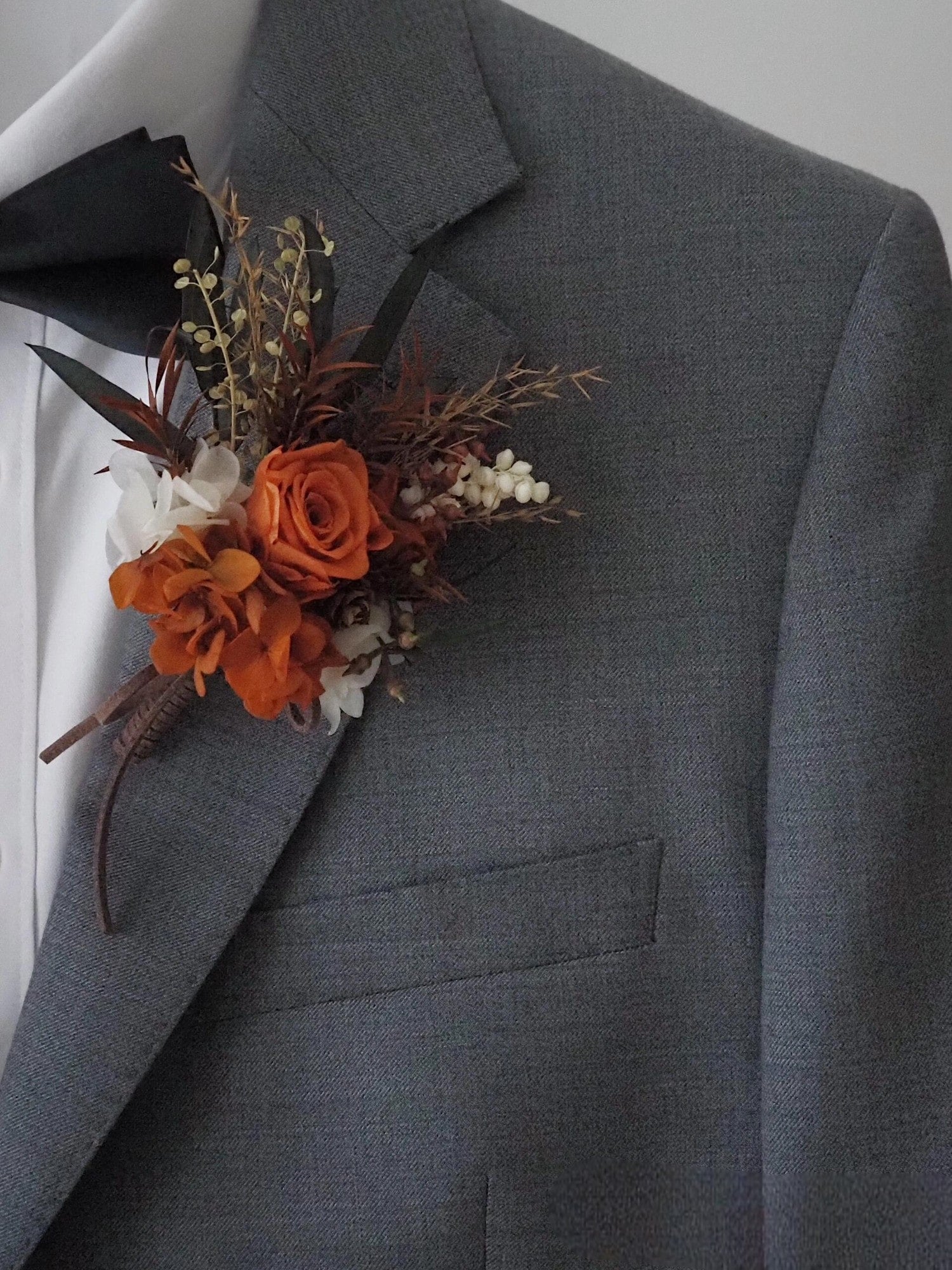 Sunset terracotta boutonniere with terracotta rose and greenery on a white plate