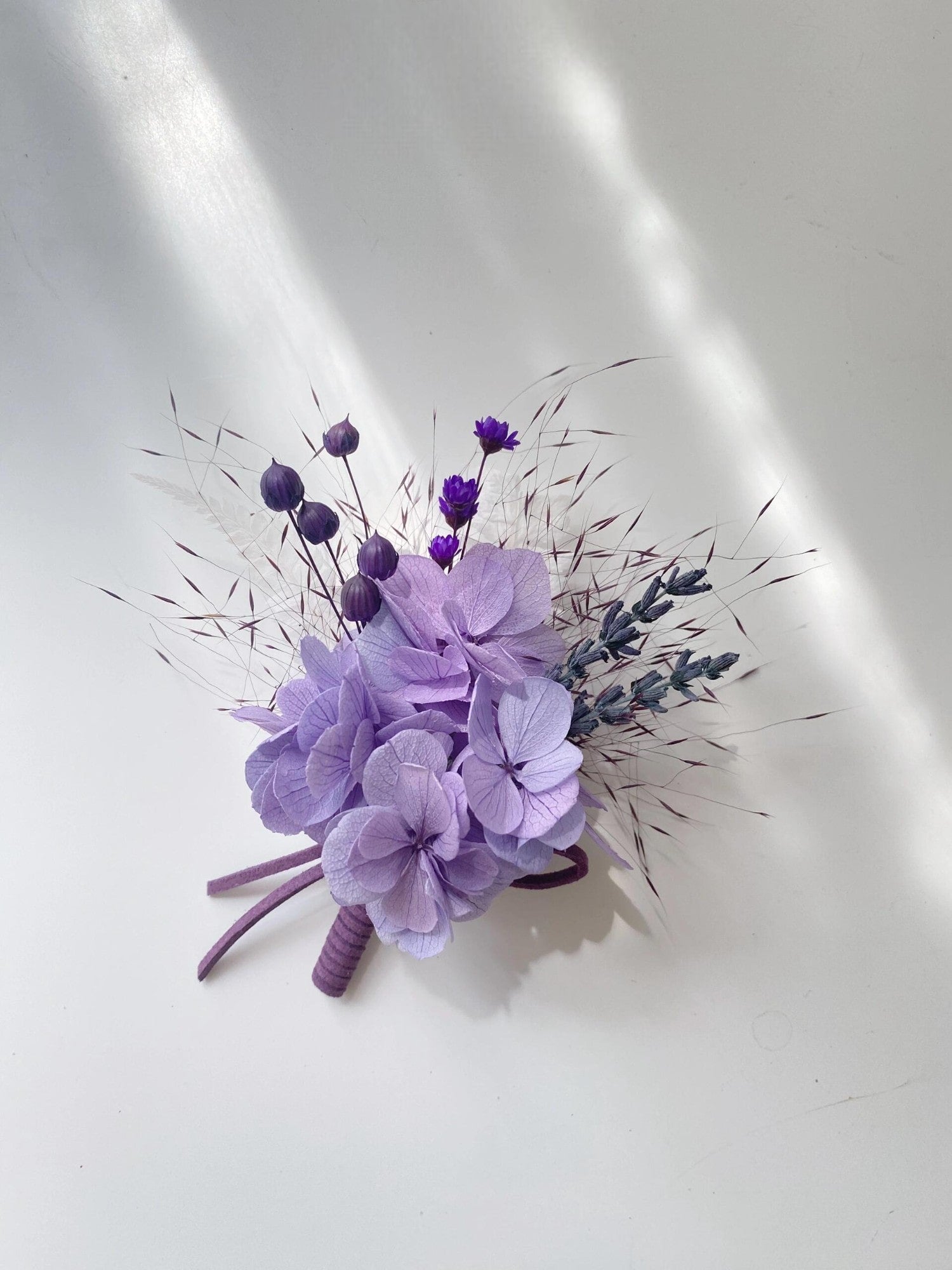 Lavender and purple hydrangea boutonniere with greenery on a white plate.
