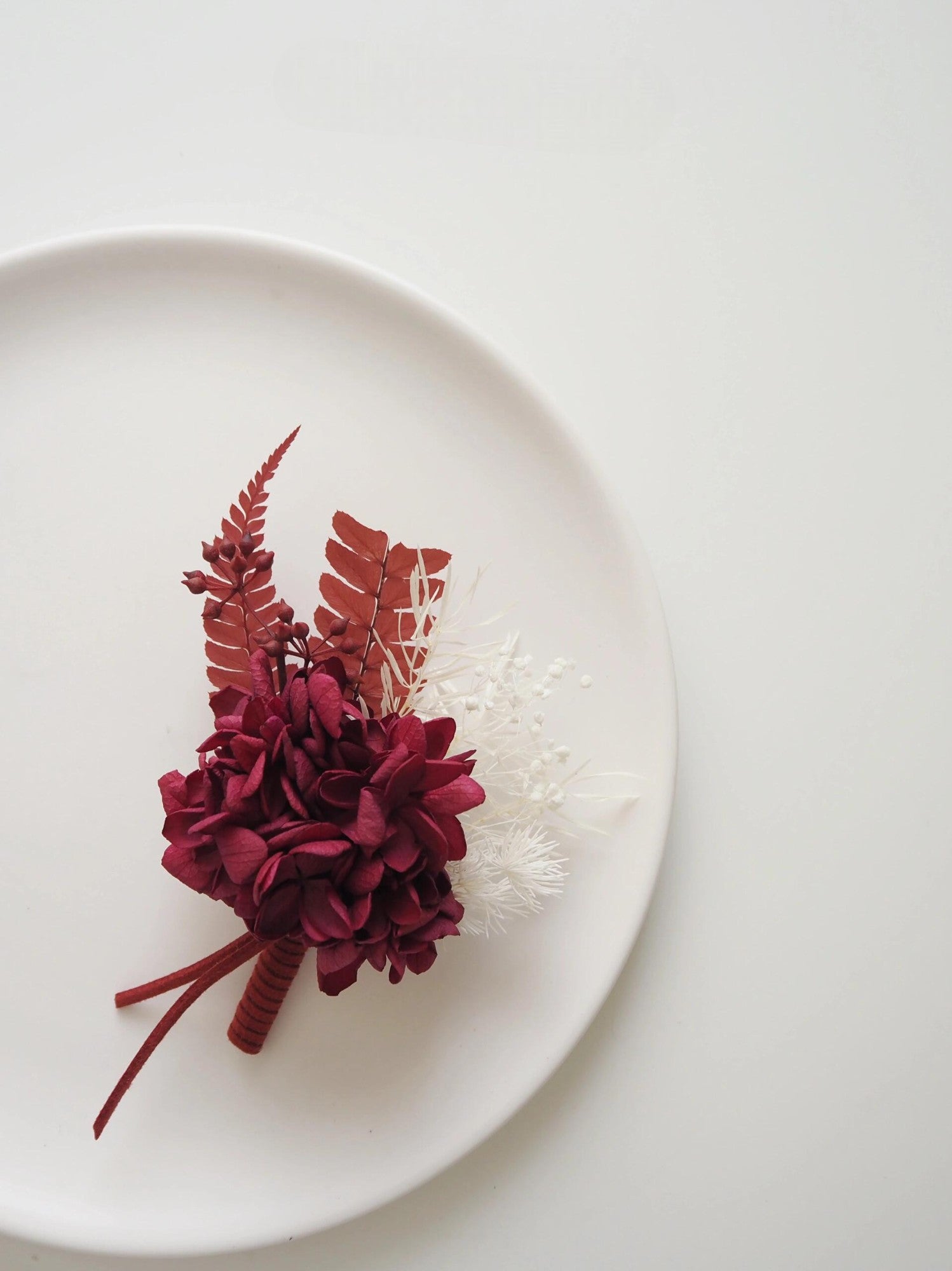 Preserved flower boutonniere featuring deep burgundy hydrangeas and white accents
